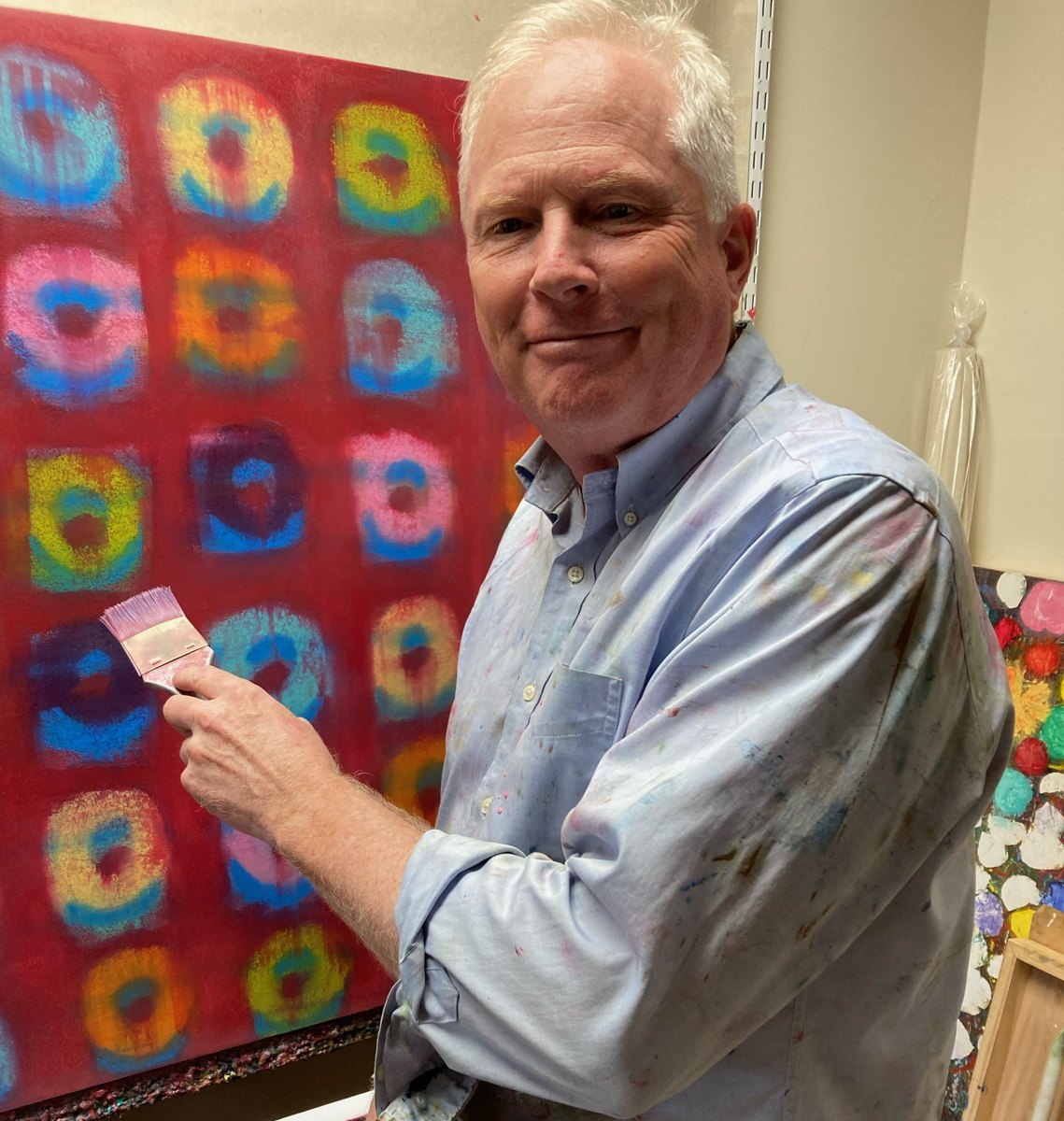 Wynn Gay in the studio, holding a paintbrush in front of a large red loop painting